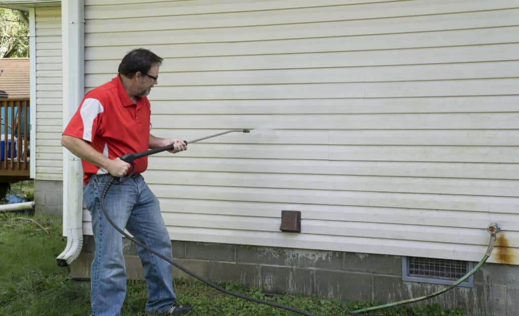 Contractor using a high pressure washer to remover algae and mold from a house with vinyl siding. Soft Washing Siding