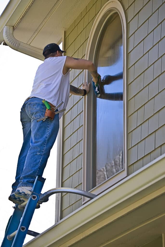 Man on a tall ladder cleaning the window on a house. Professional Residential Window Washing