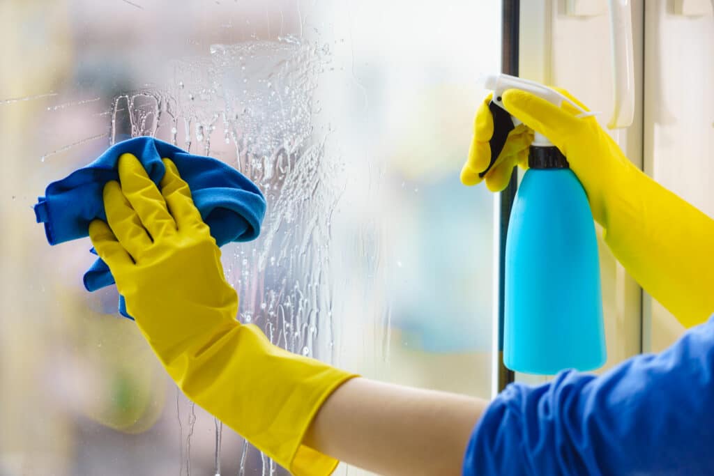 Female hand in yellow gloves cleaning window pane with rag and spray detergent. Cleaning concept. Residential Window Cleaning